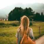A woman with blonde hair and a backpack explores a scenic mountain landscape at sunset, capturing a sense of freedom and travel.